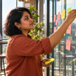 Bangladeshi professional arranging labeled task cards on a glass planning wall.